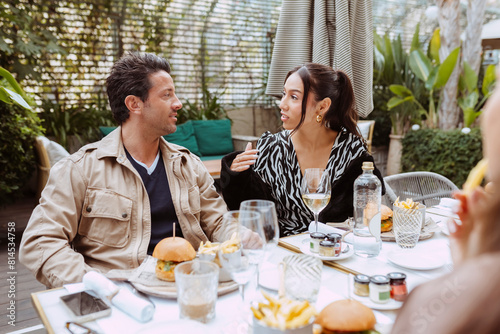 Group of young multiracial stylish handsome friends having lunch and chatting sitting on the terrace of a restaurant outdoors.