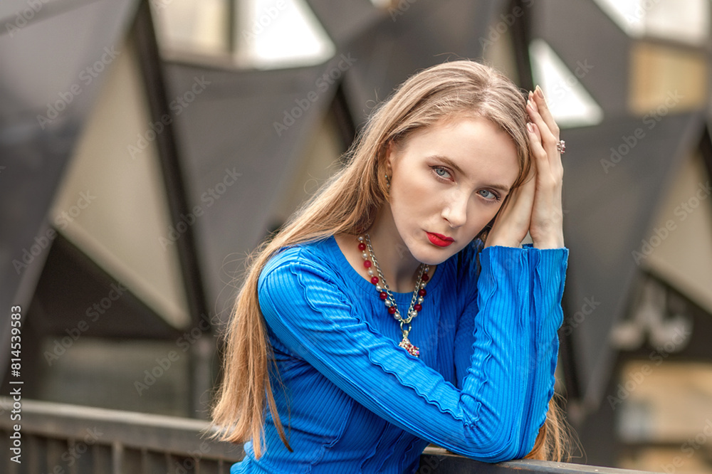 An elegant girl poses in a blue dress on a bridge between buildings on the street. An elegant girl poses in a blue dress on a bridge between buildings on the street.