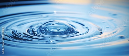 A blue water droplet falls into the water creating concentric circles and reflecting a blue wave Copy space image