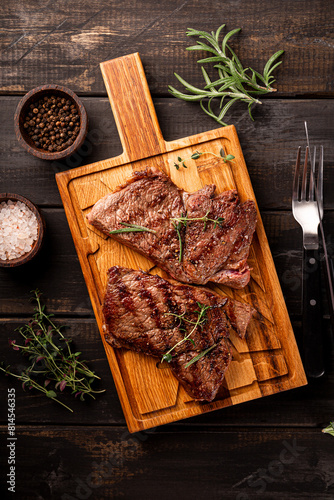 Grilled beef steak, well done with seasons and green on a black wooden background top view vertical photo