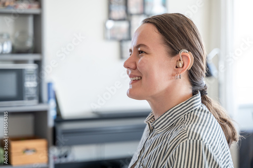 Portrait of young smiling woman with hearing aid on left ear at home