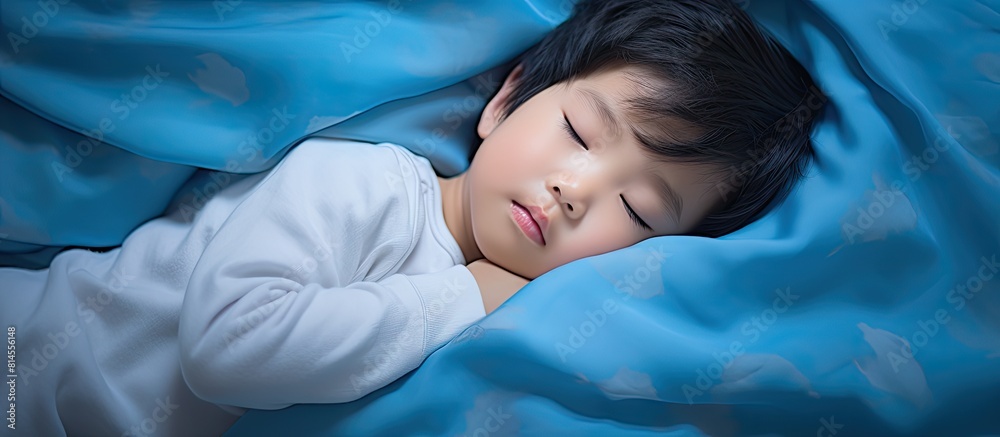 A charming young Asian toddler aged 3 4 peacefully rests on a blue pillow in bed wearing pajamas This delightful image embodies the concept of bedtime for children and offers space for copy A charming young Asian toddler aged 3 4 peacefully rests on a blue pillow in bed wearing pajamas This delightful image embodies the concept of bedtime for children and offers space for copy