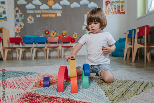 Little boy playing with rainbow wooden toy sitting on the floor in kindergarten