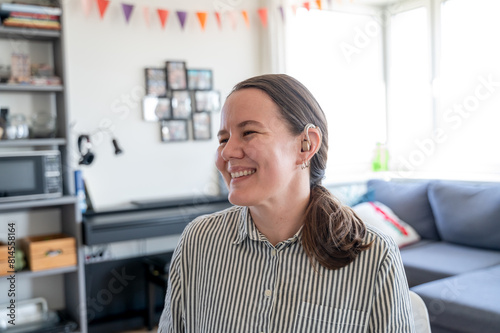 Portrait of young smiling woman with hearing aid on left ear at home