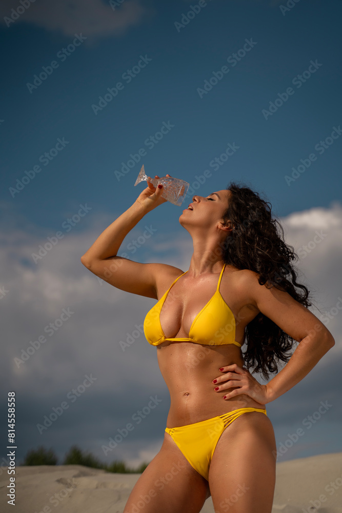 Amazing attractive woman in yellow bikini pouring water on herself from wine glass Amazing attractive woman in yellow bikini pouring water on herself from wine glass