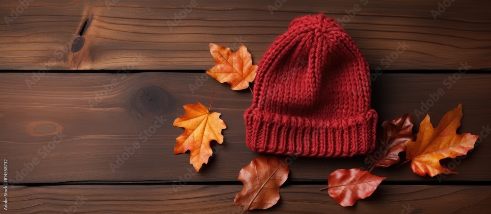 Top view of a newborn hat for little children placed on a wooden background with autumn leaves surrounding it This copy space image provides a flat lay perspective Top view of a newborn hat for little children placed on a wooden background with autumn leaves surrounding it This copy space image provides a flat lay perspective
