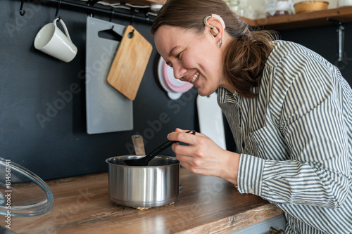 Portrait of young smiling woman with hearing aid on left ear cooking at home