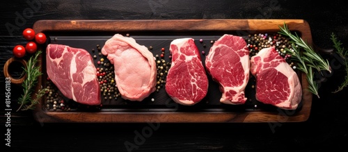 A top down view of raw lamb meat chops and steaks arranged on a wooden tray against a black background providing ample space for text or graphics