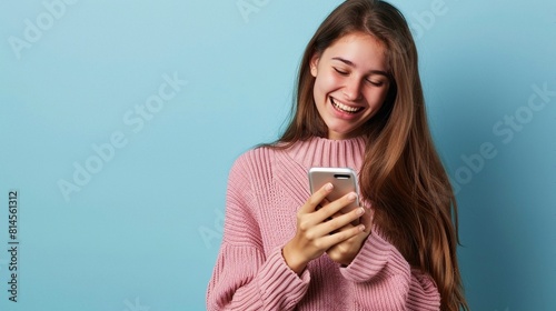 Young beautiful girl in a pink sweater using a smartphone on a blue background.