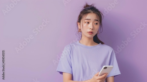 Beautiful young Asian woman confused while holding smart phone on purple background.