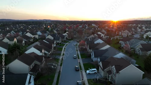 Cars in American neighborhood during sunset. Aerial rising shot revealing sprawling suburb with hundreds of houses and homes. Bright orange sunburst. photo