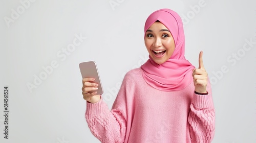 Asian muslim woman using mobile phone and pointing at the copy space on top on white background.