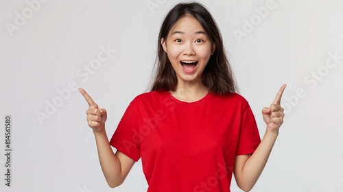 Excited young asian woman in red t-shirt pointing fingers up at copy space.