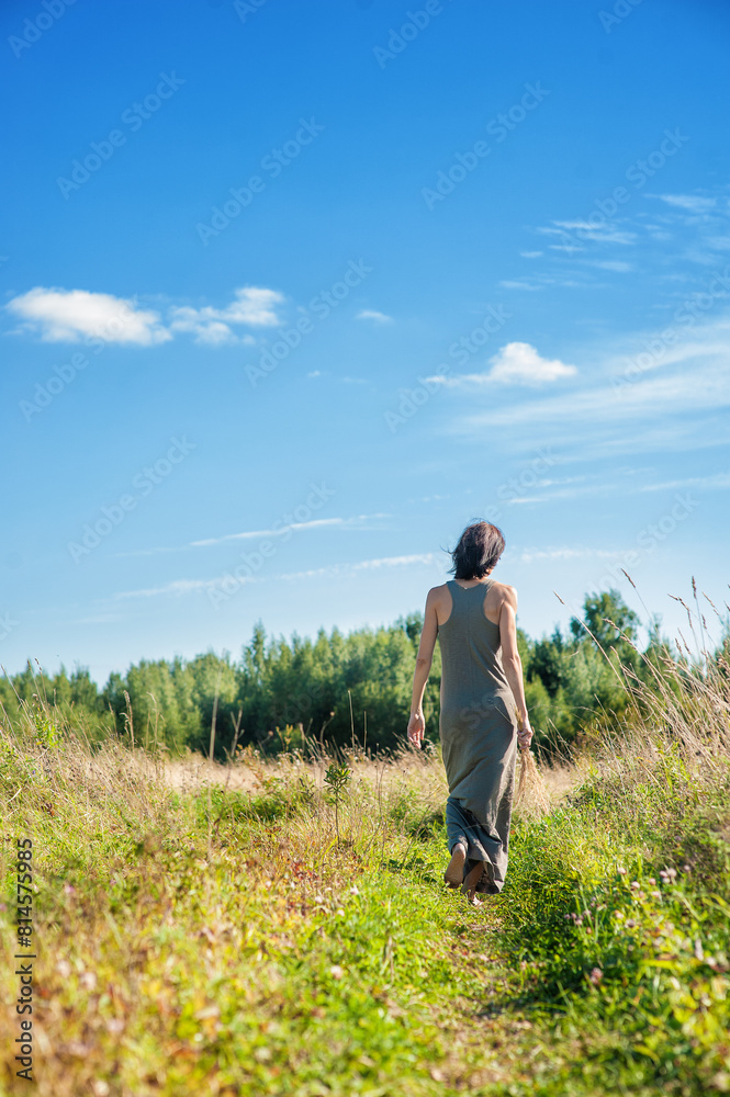 Back view of beautiful woman walking on the meadow in summer Back view of beautiful woman walking on the meadow in summer