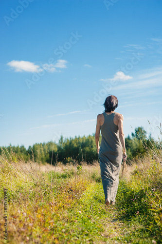 Back view of beautiful woman walking on the meadow in summer