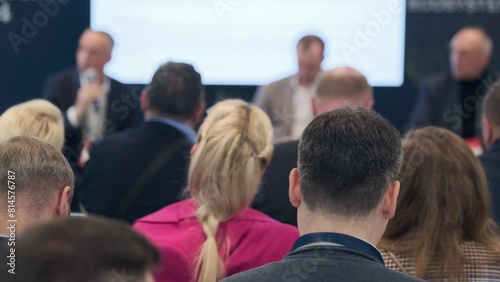 Captured moment at a business conference where speakers engage with an attentive audience, discussing professional topics in a corporate setting.