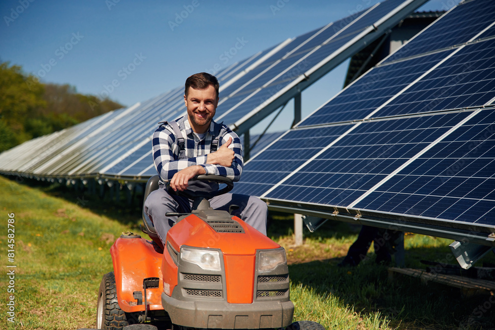 Rides a lawnmower. Engineer with photovoltaic solar panels outdoors at daytime Rides a lawnmower. Engineer with photovoltaic solar panels outdoors at daytime