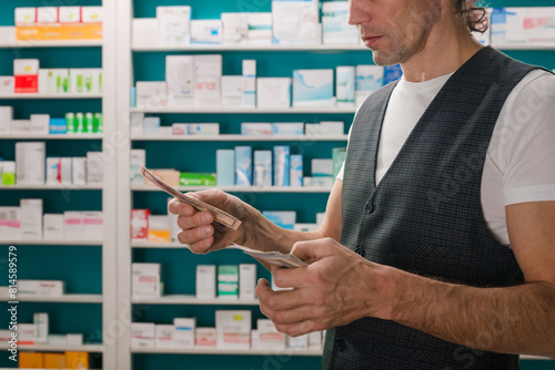 Cropped photo of male customer paying for medicine using cash. Customer payment: Man pays with cash at the pharmacy photo