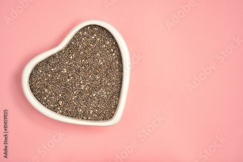 Photograph of chia seeds in heart shape white bowl with copy space on pink colour background. Top view. Health care concept.