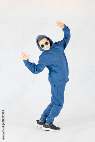 Cheerful boy in a blue tracksuit and sunglasses. Pretty boy,. Baby model. A little boy poses on a white background.