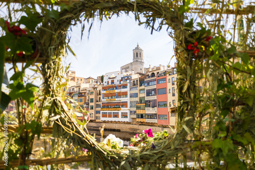 Girona, Spain - May 13th, 2024: TEMPS DE FLORS - Flower Time Festival. View of the Cathedral and the colorful houses of the Onyar river in a plants frame with flowers