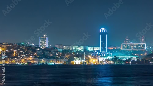 Night timelapse view of besiktas district with some illuminated skyscrapers and mosque in Istanbul taken from asian part of the city. Reflection on Bosphorus water photo