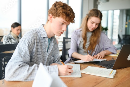students sit at shared desk making notes studying together at university
