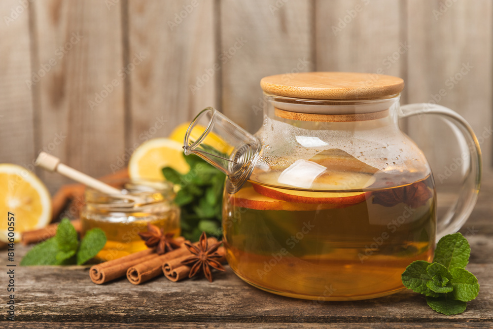 Fragrant hot tea with cinnamon stick and anise on a textured wooden background. A teapot brewing hot tea with honey, lemon, mint and apples. Spicy tea with spices. Immunity tea. Health concept. Fragrant hot tea with cinnamon stick and anise on a textured wooden background. A teapot brewing hot tea with honey, lemon, mint and apples. Spicy tea with spices. Immunity tea. Health concept.