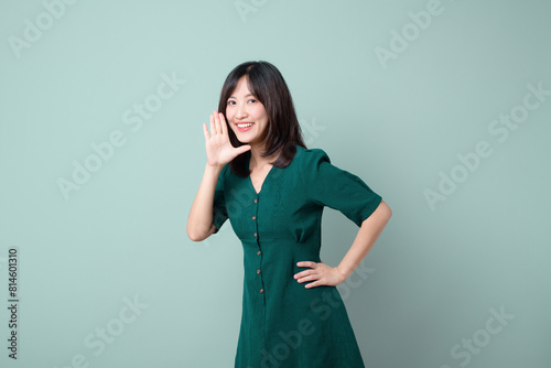 Happy Asian woman shouting above green dress poses against green background blank copy space for advertising content promotion