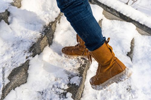 Slippery stairs in winter after heavy snowfall. Feet shod in winter shoes on snowy steps. Somebody climbs the stairs close up view. The stairs were not cleared. photo