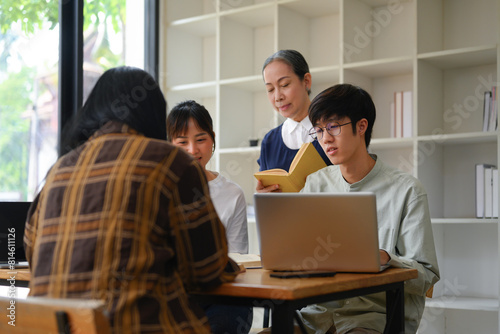 Happy mature professor helping group of students at university library