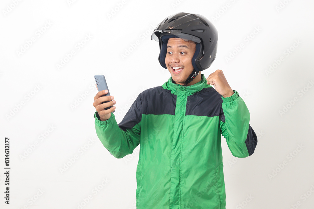 Portrait of Asian online taxi driver wearing green jacket and helmet using mobile phone while raising his fist and celebrating success. Isolated image on white background Portrait of Asian online taxi driver wearing green jacket and helmet using mobile phone while raising his fist and celebrating success. Isolated image on white background
