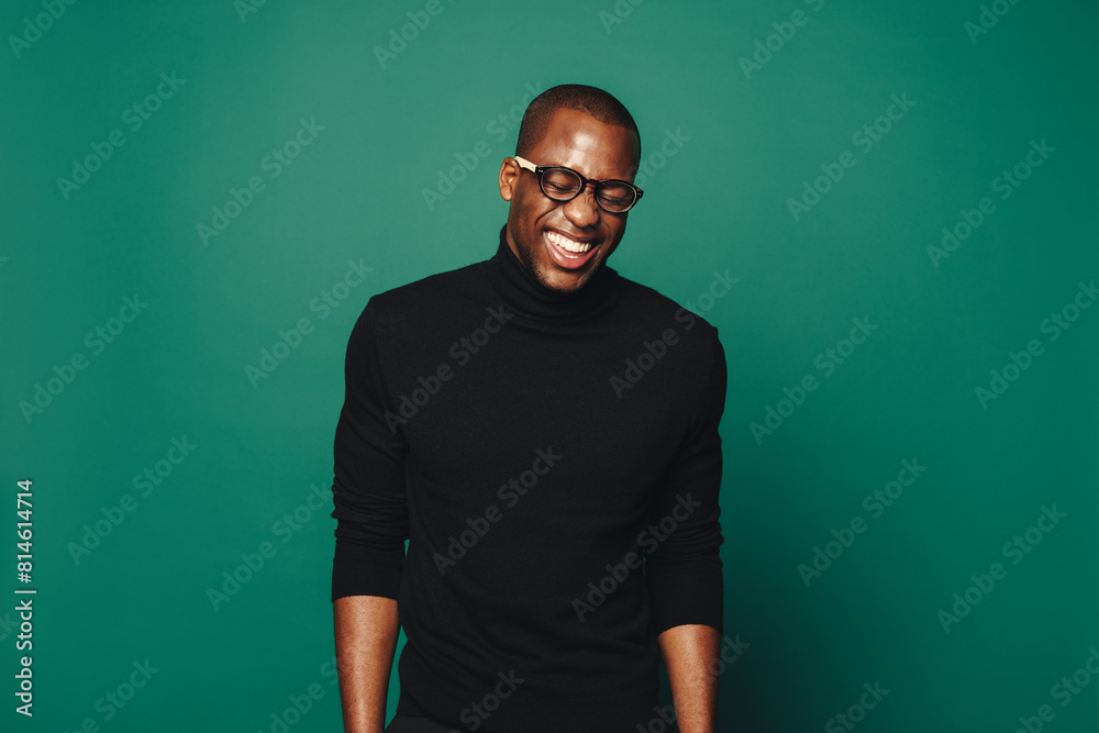 Confident African man laughing while standing against green background