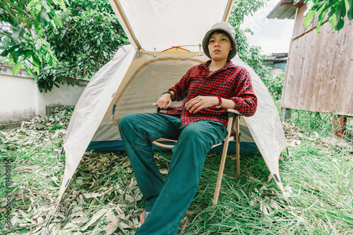 A real transgender Asian lesbian enjoys alone, smiling in relaxation while sitting outdoors near a tent