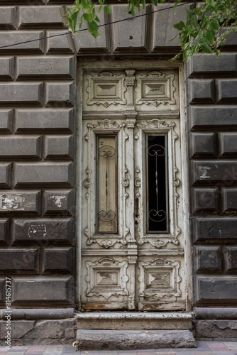 Ancient wooden door standing in contrast to the modern Armenian architecture of the surroundings © Wirestock