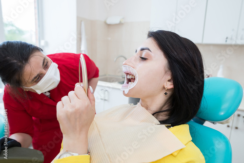 A dentist demonstrates a patient's perfect smile after implanting dental veneers or teeth whitening.