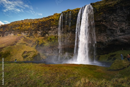 people standing near the side of a tall waterfall in iceland