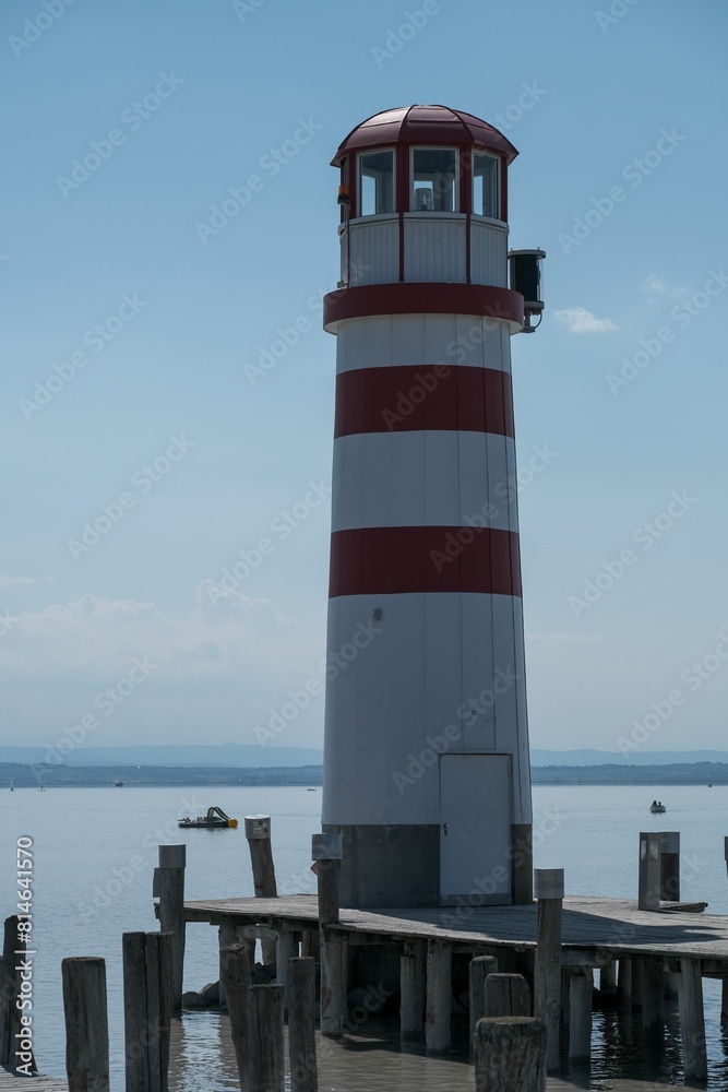 a red and white light house on the pier in front of a boat a red and white light house on the pier in front of a boat