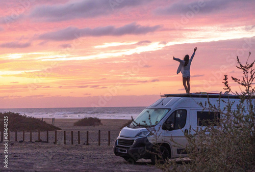 Happy person on camper van roof, embracing sunset by the sea, capturing the essence of travel freedom and adventurous spirit