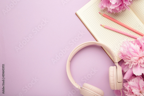 Modern pink headphones with flowers peonies and notebook on purple background