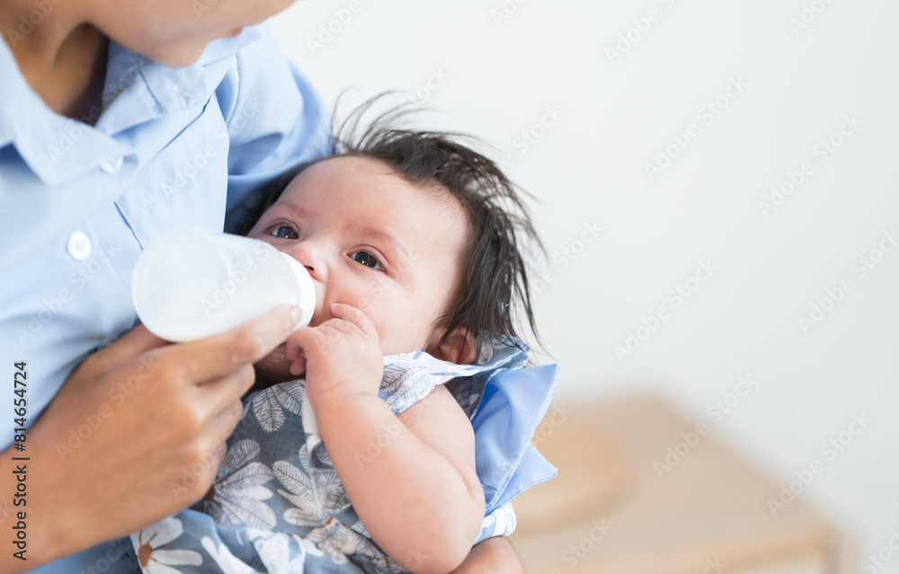 Asian woman feeding milk her cute mixed race little newborn 3 months old baby girl from bottle. Mother holding adorable small daughter in warm arms at home. Copy space Asian woman feeding milk her cute mixed race little newborn 3 months old baby girl from bottle. Mother holding adorable small daughter in warm arms at home. Copy space