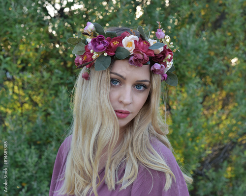 close up portrait of pretty blonde female model wearing a flower crown wreath and purple dress.  green nature  plants and trees in background