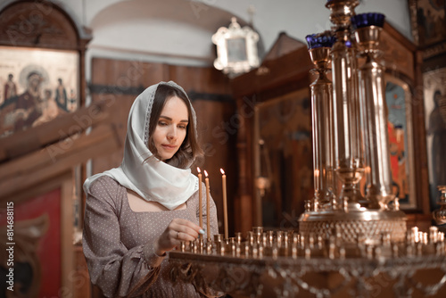 Young beautiful woman in the Orthodox Church lit candles in a candlestick