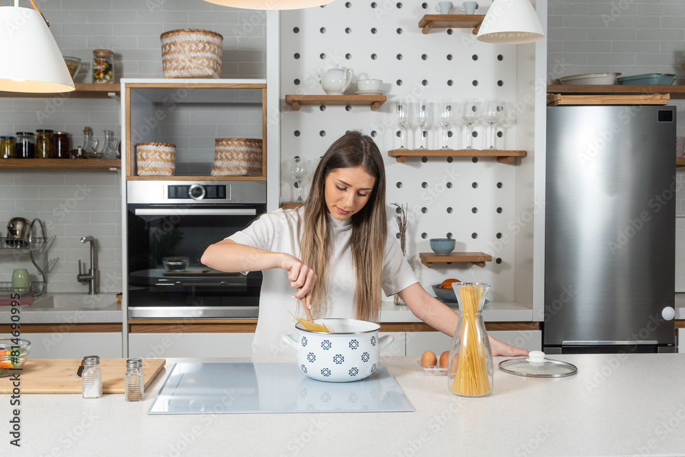 Cooking - Young woman with spaghetti on stove cooking Italian cuisine. University student or business woman making a lunch in domestic kitchen. Fast preparation of food on busy day.