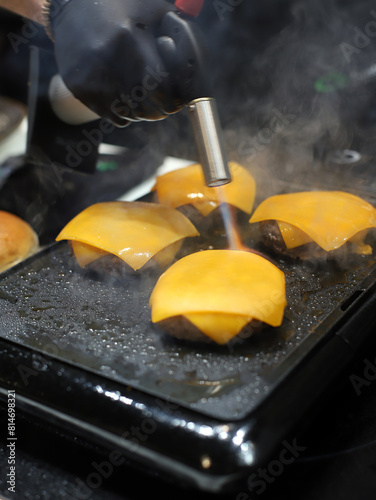 chef cocinando hamburguesas de carne y queso fundido con soplete de cocina photo