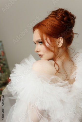 The woman with long red hair is donning a white gown with ruffled sleeves. She has a bun on her head, complemented by a bridal headpiece
