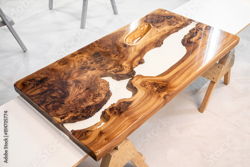 Live edge elm burl slab table top with central epoxy resin river on sawhorses in professional workshop