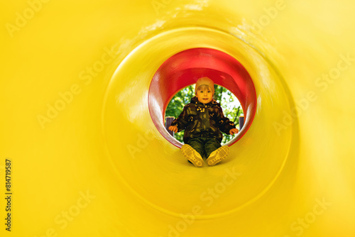 Active little girl inside a tube slide on playground. Cute little girl sliding down on slide. Healthy activity for children. Child on yellow background with free space for text. Childhood concept.