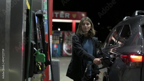 A woman fills the car with fuel in the evening at the gas station, pump filling fuel nozzle in fuel tank of car, high price of petrol and oil fuel, economic concept photo