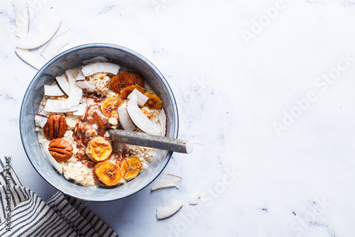 Overnight oatmeal with chocolate, pecans, coconut chips and dried banana, white background.